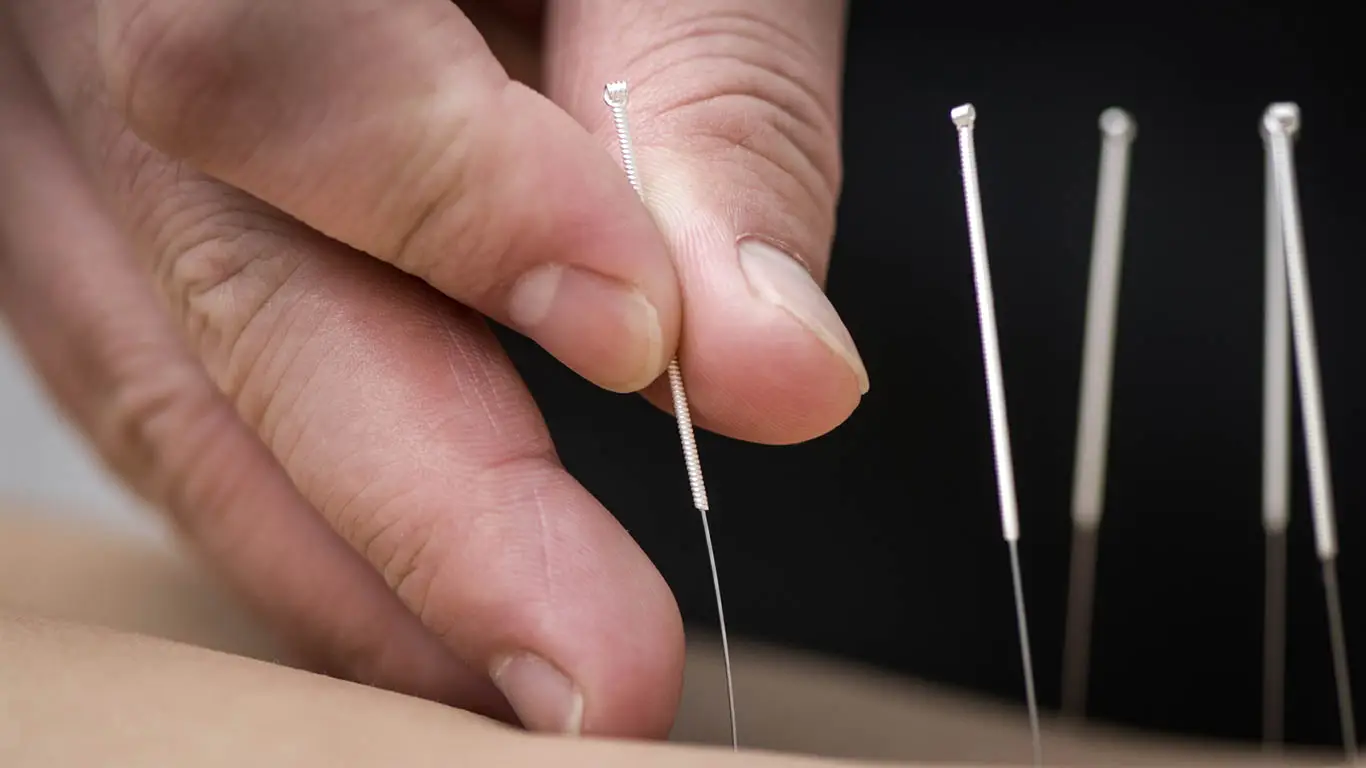 Gros plan d'une main tenant une aiguille d'acupuncture prête à être utilisée. Intuci, Médecine Traditionnelle Chinoise, Genève.